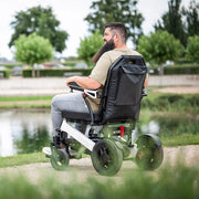 Kräftiger Mann fährt mit dem ergoflix heavy Elektrorollstuhl in Weiß-Schwarz an einem Teich entlang und genießt die Natur – Seitenansicht