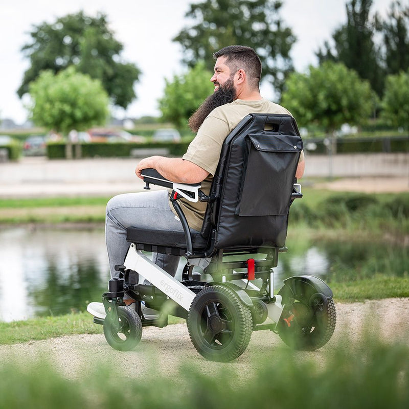 Kräftiger Mann fährt mit dem ergoflix heavy Elektrorollstuhl in Weiß-Schwarz an einem Teich entlang und genießt die Natur – Seitenansicht