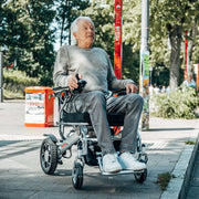 Älterer Mann fährt mit dem ergoflix basic Elektrorollstuhl selbstständig auf einem Bürgersteig und bedient den Joystick mit einer Hand
